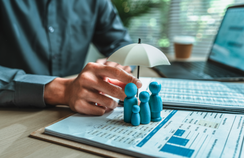 Man sitting at desk, holding a white umbrella above blue figurines