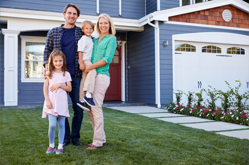 Smiling family standing in front of house