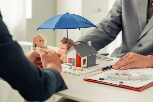 Two people sitting at a desk, one holding an umbrella over a model house