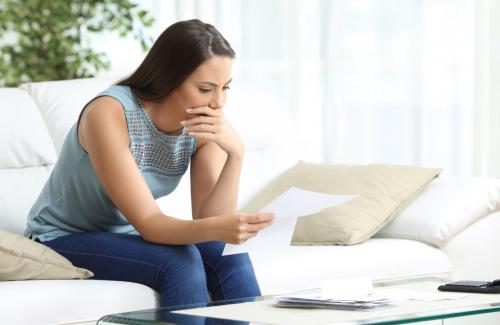 Worried woman sitting on couch and reviewing documents