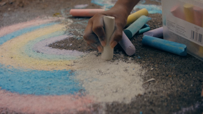 a person's hand drawing on the sidewalk with colored chalk