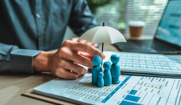 Man sitting at desk, holding a white umbrella above blue figurines