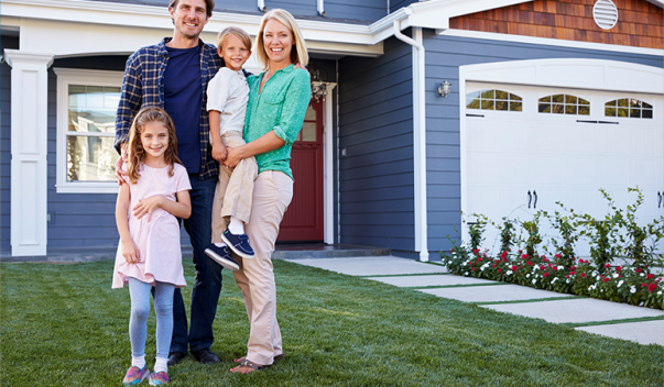 Smiling family standing in front of house