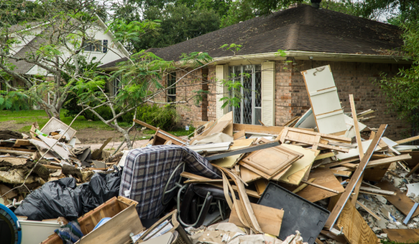 Suburban house with flood debris and trash piled up in the front yard