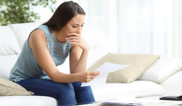Worried woman sitting on couch and reviewing documents